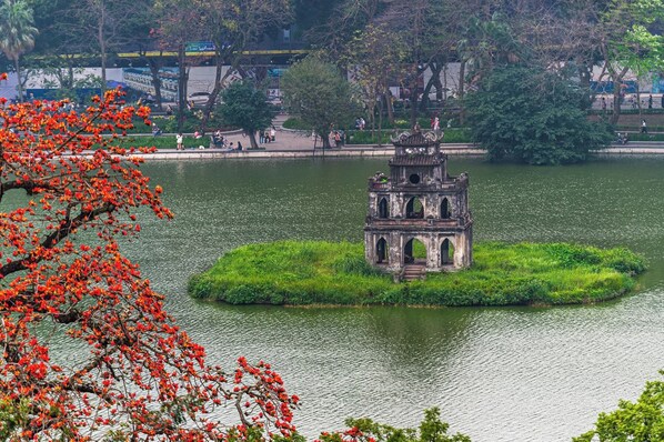 A historic tower on an island in a lake, surrounded by lush greenery and trees.
