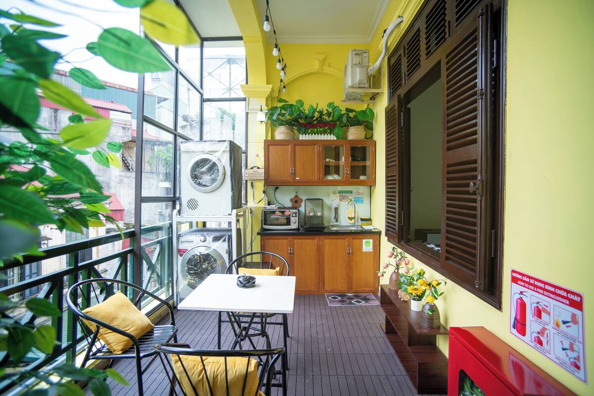Ein Balkon mit Tisch und Stühlen, eine kleine Küchenzeile mit Schränken und Geräten sowie Blick auf umliegende Gebäude.