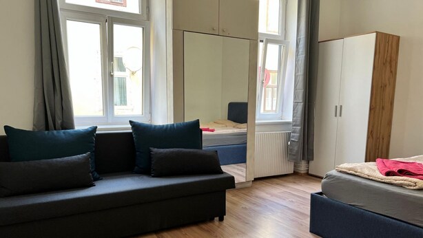 Ein Zimmer mit Sofa, Bett, Kleiderschrank und einem Fenster mit Vorhängen.
