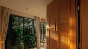 A modern interior with a sliding glass door leading to a lush garden, a wooden panel wall, and a clean tiled floor. - Exclusive villa in Botanica The Nature (Choeng Thale)