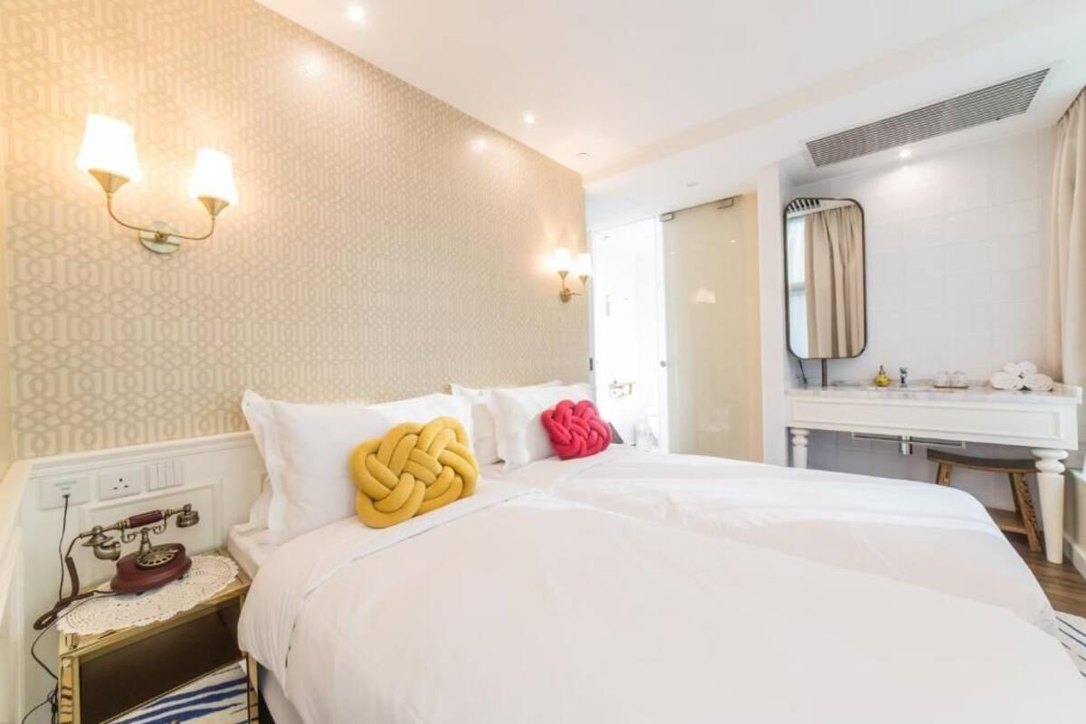 A hotel room with a bed, bedside table, lamp, and a mirror above the sink.