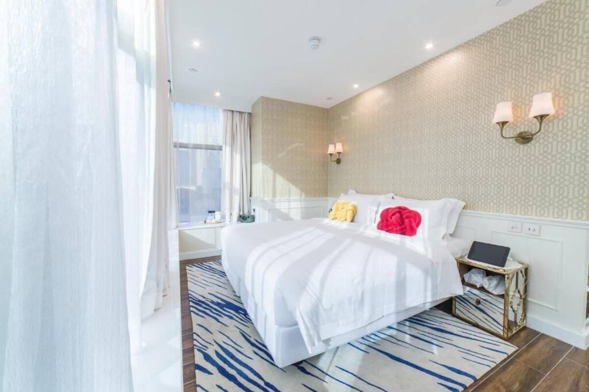 A modern hotel room with a large bed, a bedside table with a laptop, and a patterned wall.