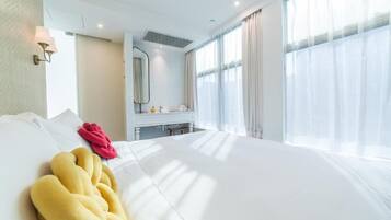 A hotel room with a large bed, a bedside table, a mirror, and a window with sheer curtains.