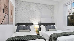 Un dormitorio con dos camas, paredes blancas, una pared de acento de ladrillo y una ventana.