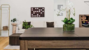 Una sala de estar moderna con una mesa de comedor de madera, un sofá blanco, un panel decorativo en la pared y una planta en maceta.