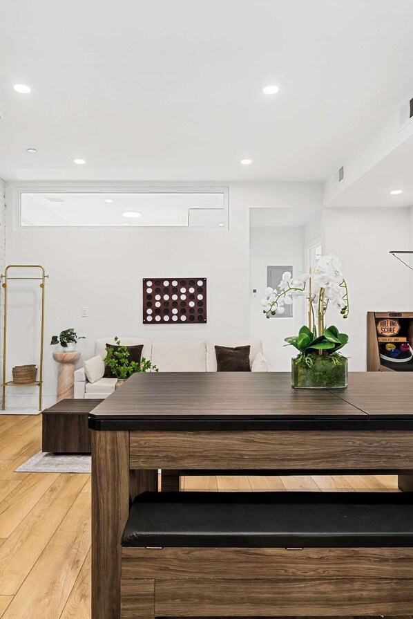 A modern living room with a wooden dining table, a white sofa, a decorative wall panel, and a potted plant.