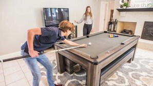 Una mesa de billar en una habitación con televisión, chimenea y alfombra estampada.