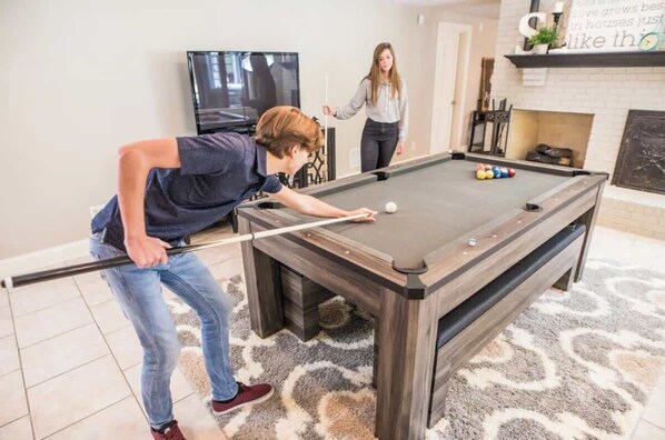 A pool table in a room with a television, a fireplace, and a patterned rug.