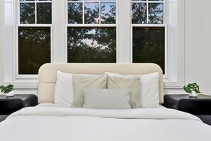A bed with a headboard, two bedside tables, and a window with a view of trees.