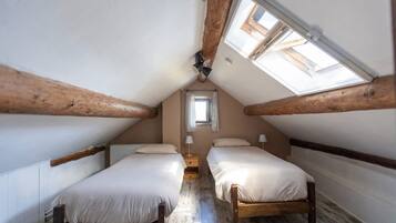 Une petite chambre mansardée avec deux lits en bois, une lucarne et une fenêtre.