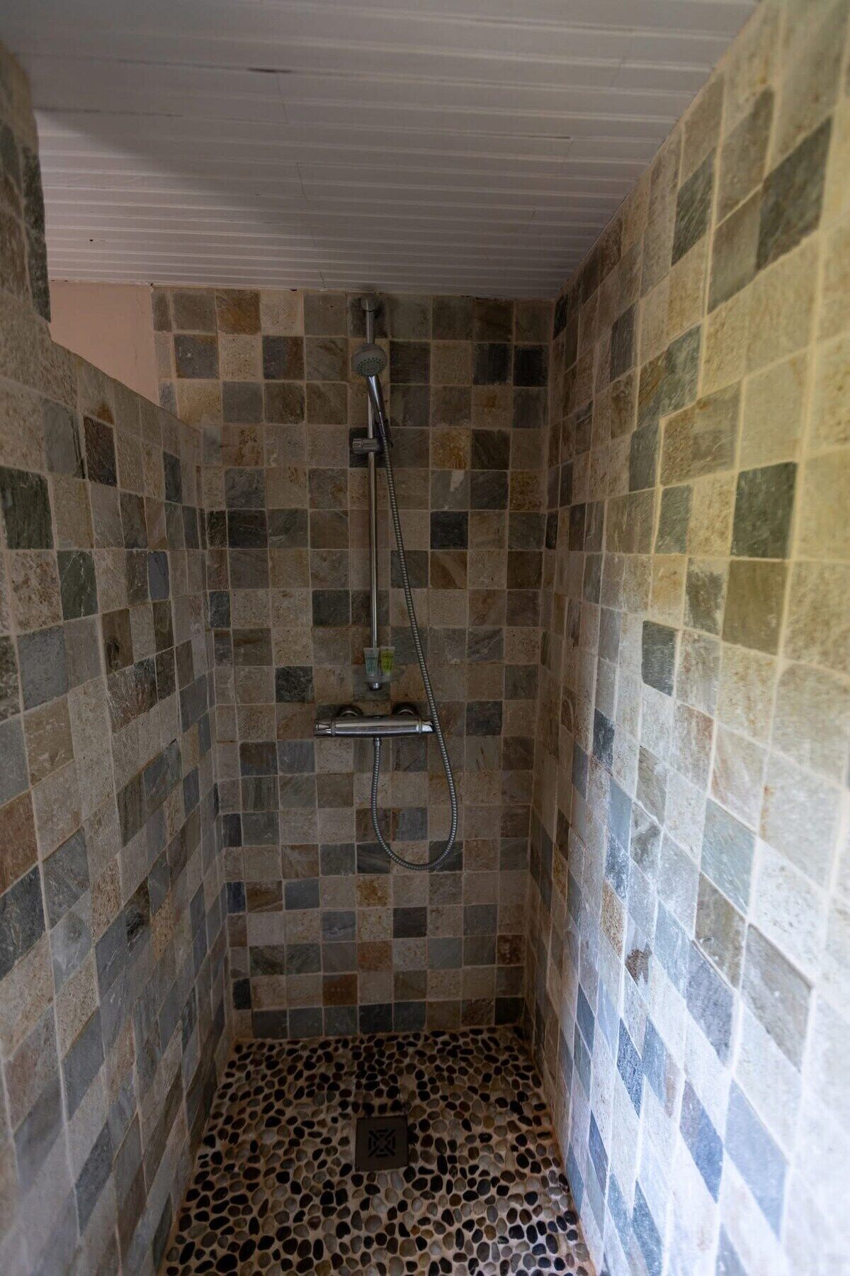 A shower with a tiled wall and floor, a handheld showerhead, and a drain.