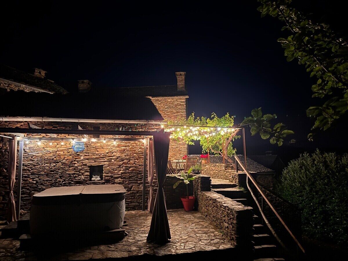 A stone building with a covered outdoor seating area, string lights, and a potted plant.
