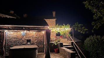 A stone building with a covered outdoor seating area, string lights, and a potted plant.