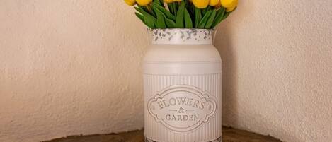 Un vase en céramique blanche orné d’un motif floral et portant l’inscription « Fleurs et jardin », contenant des tulipes jaunes.
