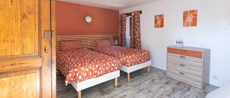 Een slaapkamer met twee bedden, een houten garderobe, een dressoir en een spiegel.