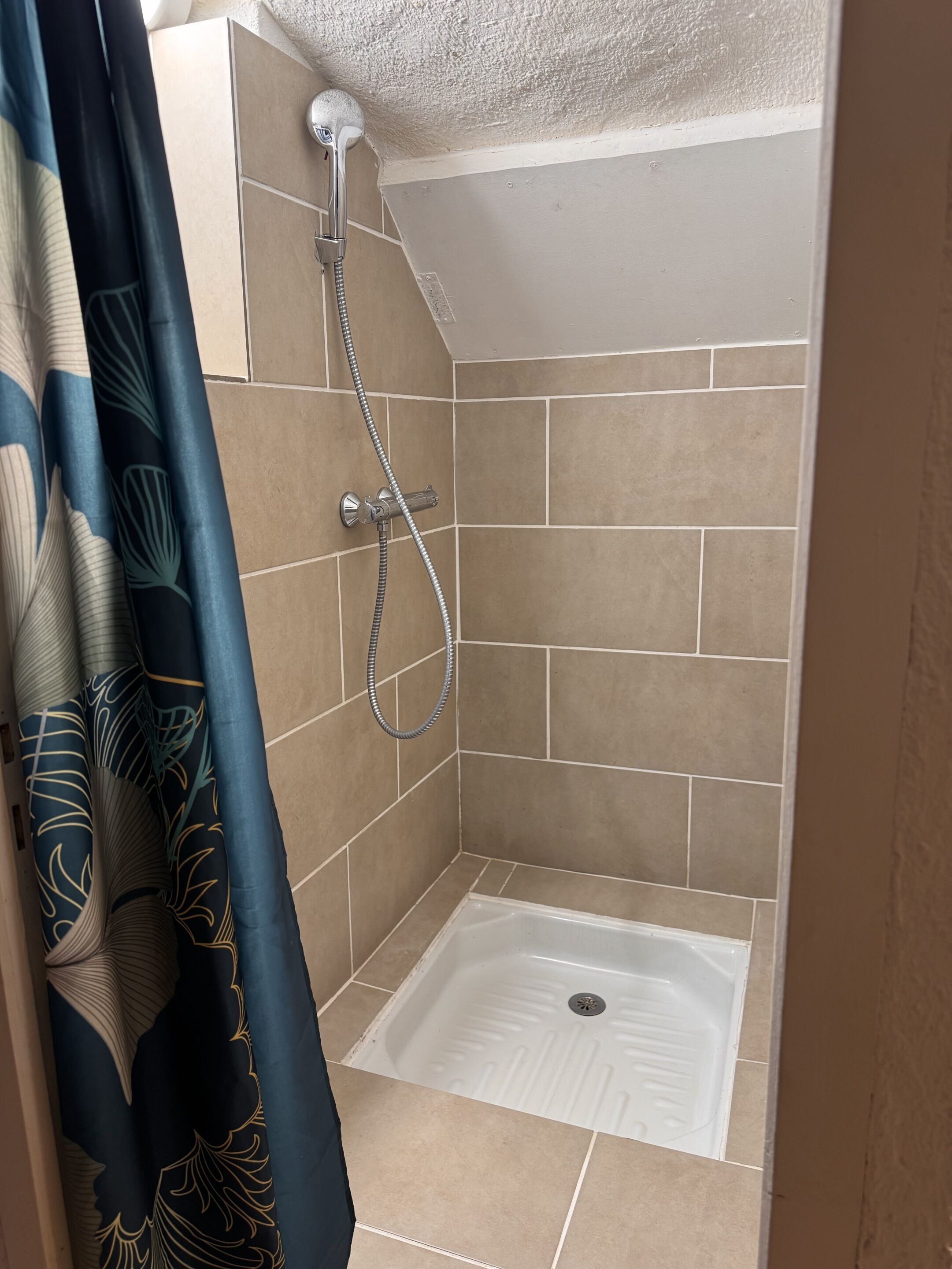 Un pequeño espacio de ducha con azulejos, con cabezal de ducha y manguera.