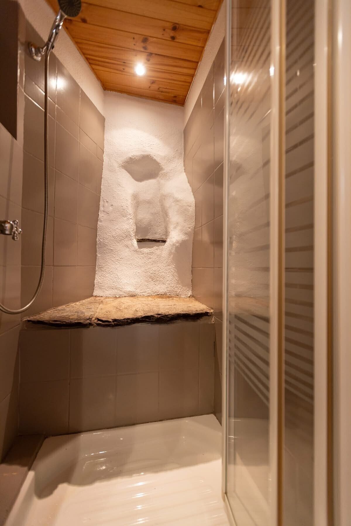 A shower area with a wooden ceiling, tiled walls, and a glass shower enclosure.