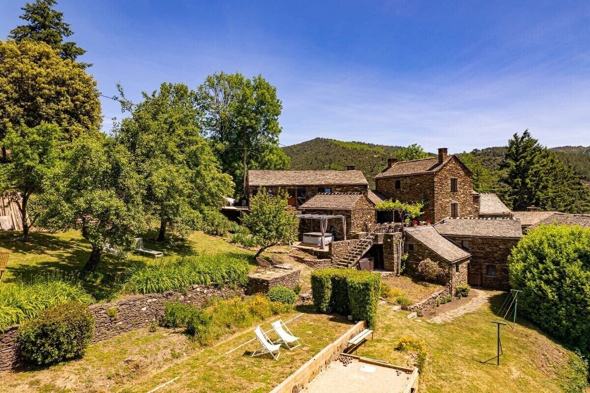 Un bâtiment en pierre comprenant plusieurs pièces, un jardin avec un banc et un ciel dégagé.