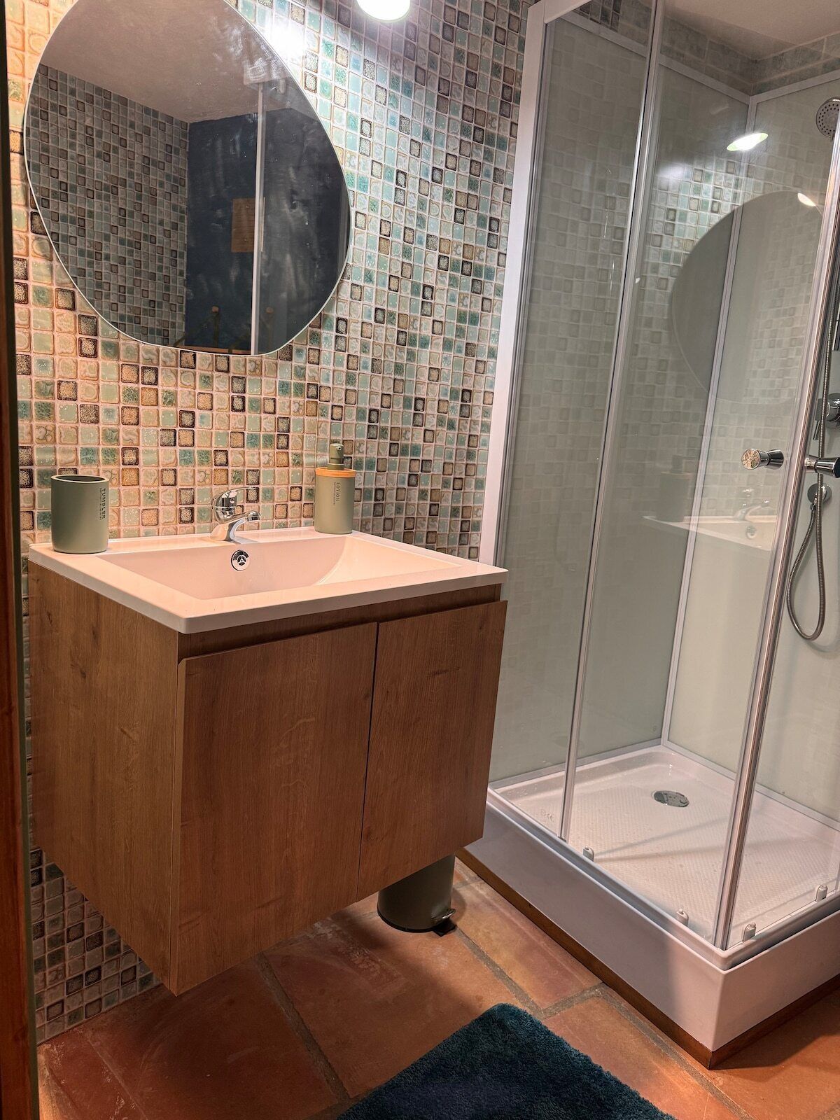 Ein Badezimmer mit gefliestem Rückspritzschutz, einem Holzbadezimmer-Möbelstück, einem Waschbecken, einem Spiegel und einer Duschkabine.