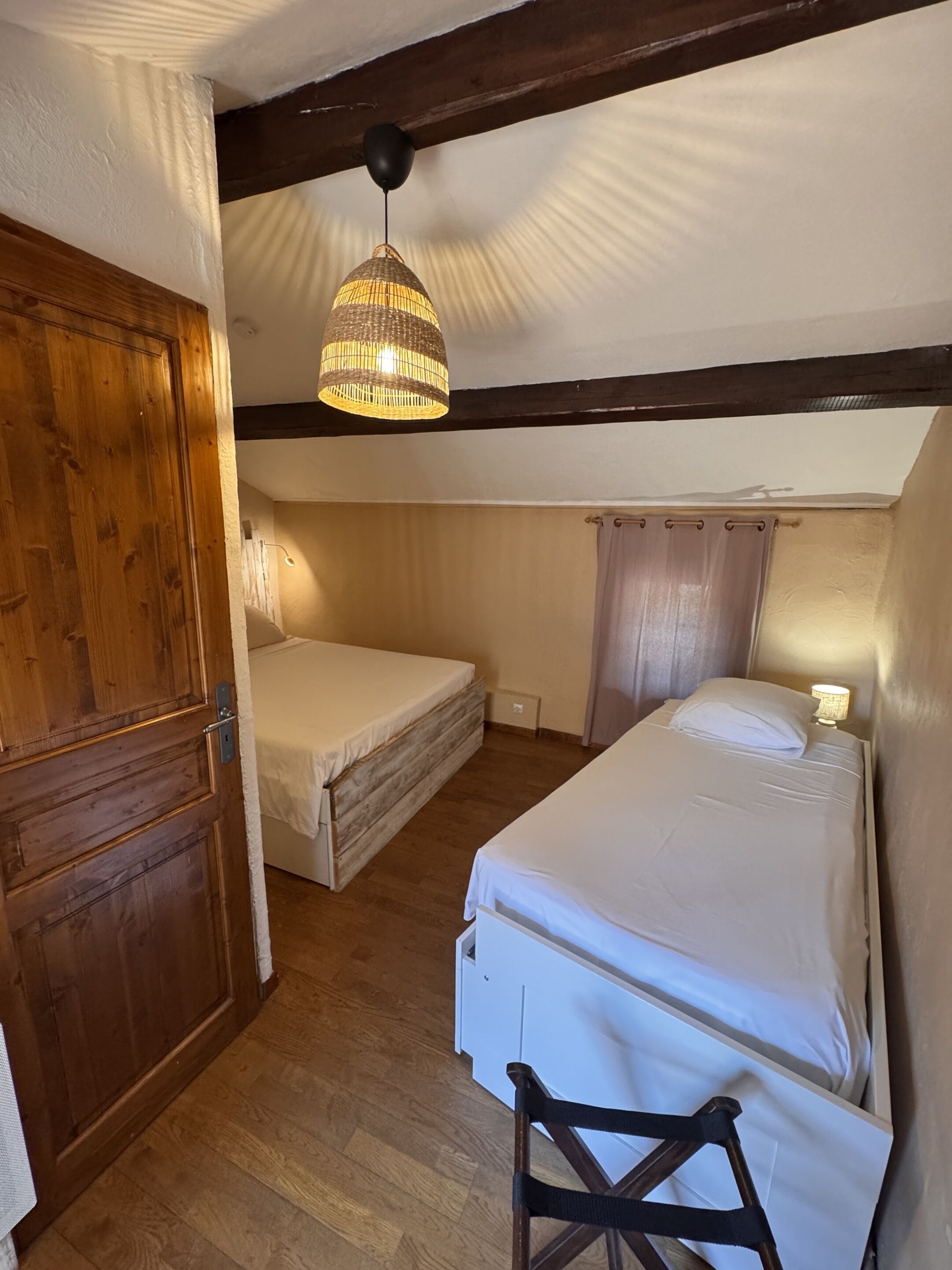 Een kamer met twee bedden, houten vloeren, een plafondventilator en een hanglamp.