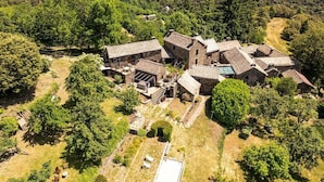 Vista aérea de una finca rústica con varias construcciones de piedra, rodeada de un bosque denso.