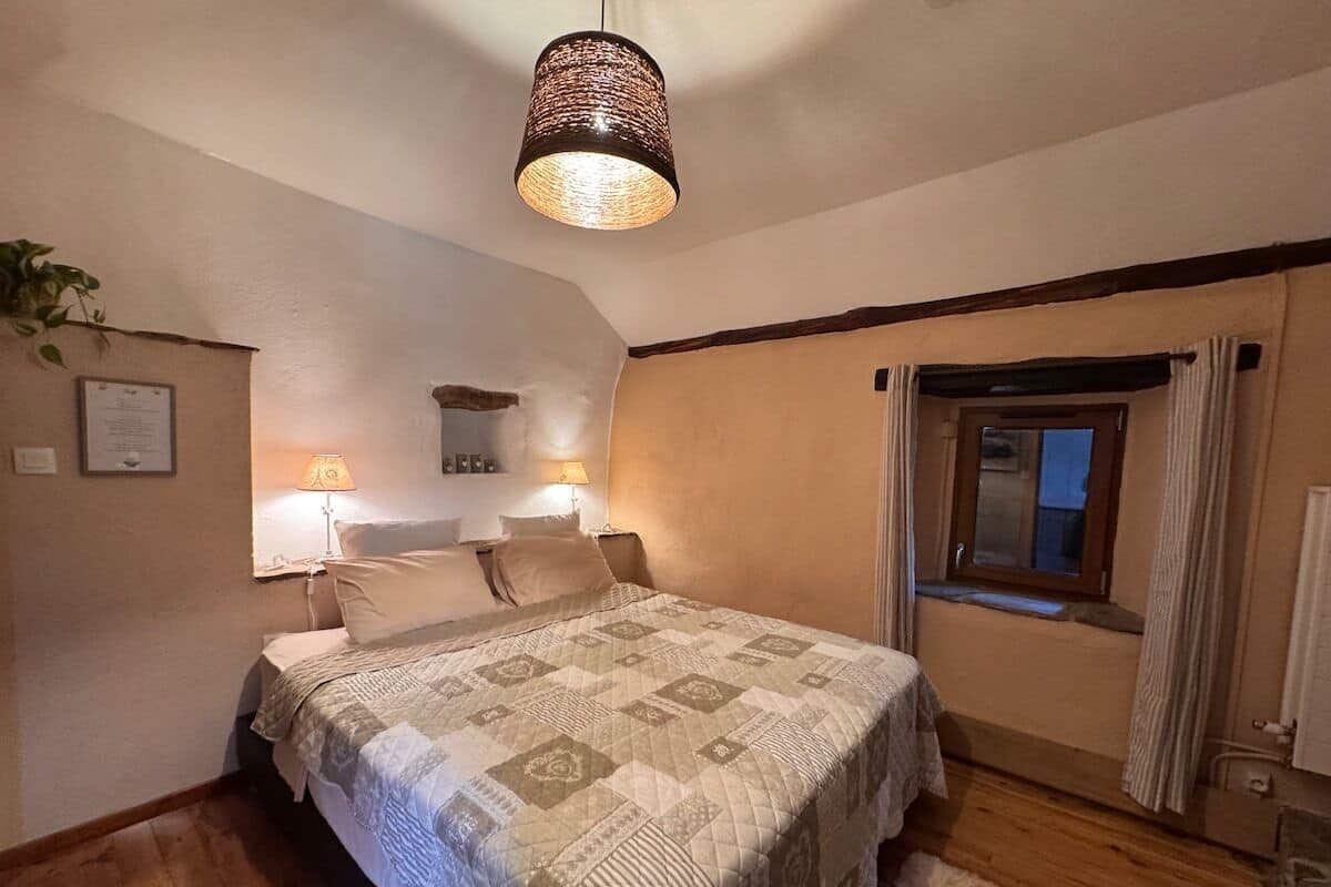 A bedroom with a bed, two bedside lamps, a window with curtains, and a ceiling light fixture.