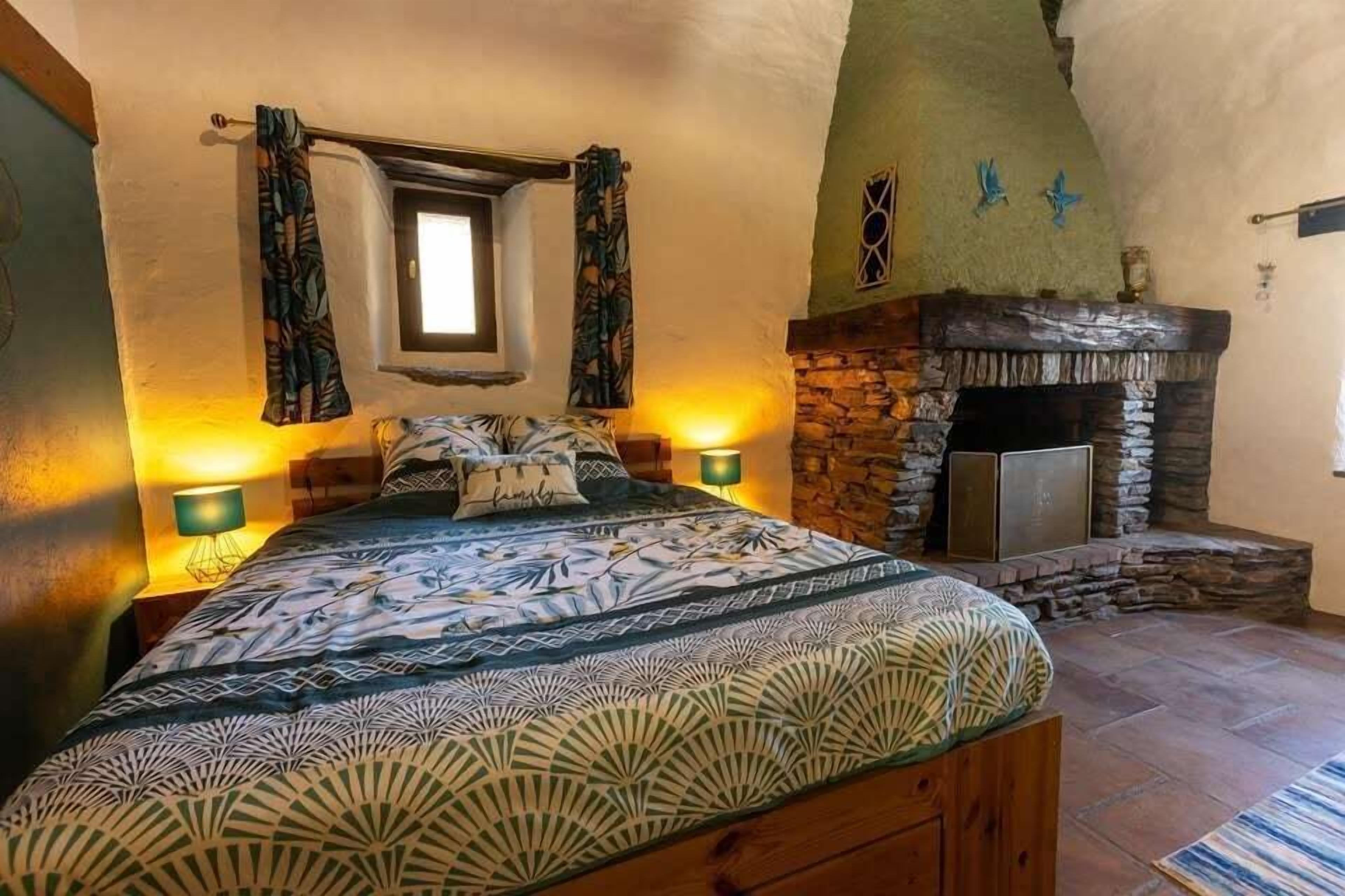 A bedroom with a bed, a stone fireplace, and two wall-mounted lamps.