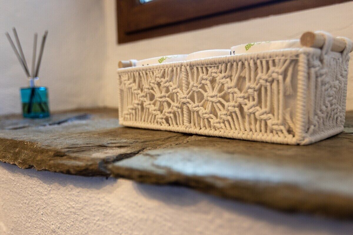 Un panier blanc, orné de motifs complexes, posé sur une surface texturée, peut-être une table ou une étagère, avec une fenêtre en arrière-plan.