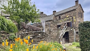 Un edificio de piedra con una escalera que conduce a la entrada, rodeado por un jardín con flores de naranja.