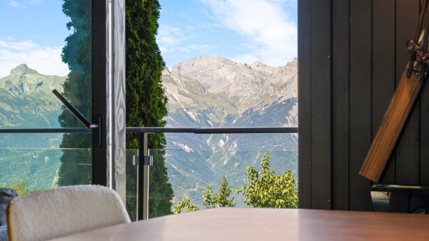 A room with a wooden table and a chair, a glass door leading to a balcony with a mountain view. - Kool Kabin - 8 pers - view, charm and comfort (Haute-Nendaz)