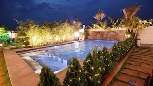 Una piscina con una cascada, rodeada de abundante follaje y palmeras iluminadas.