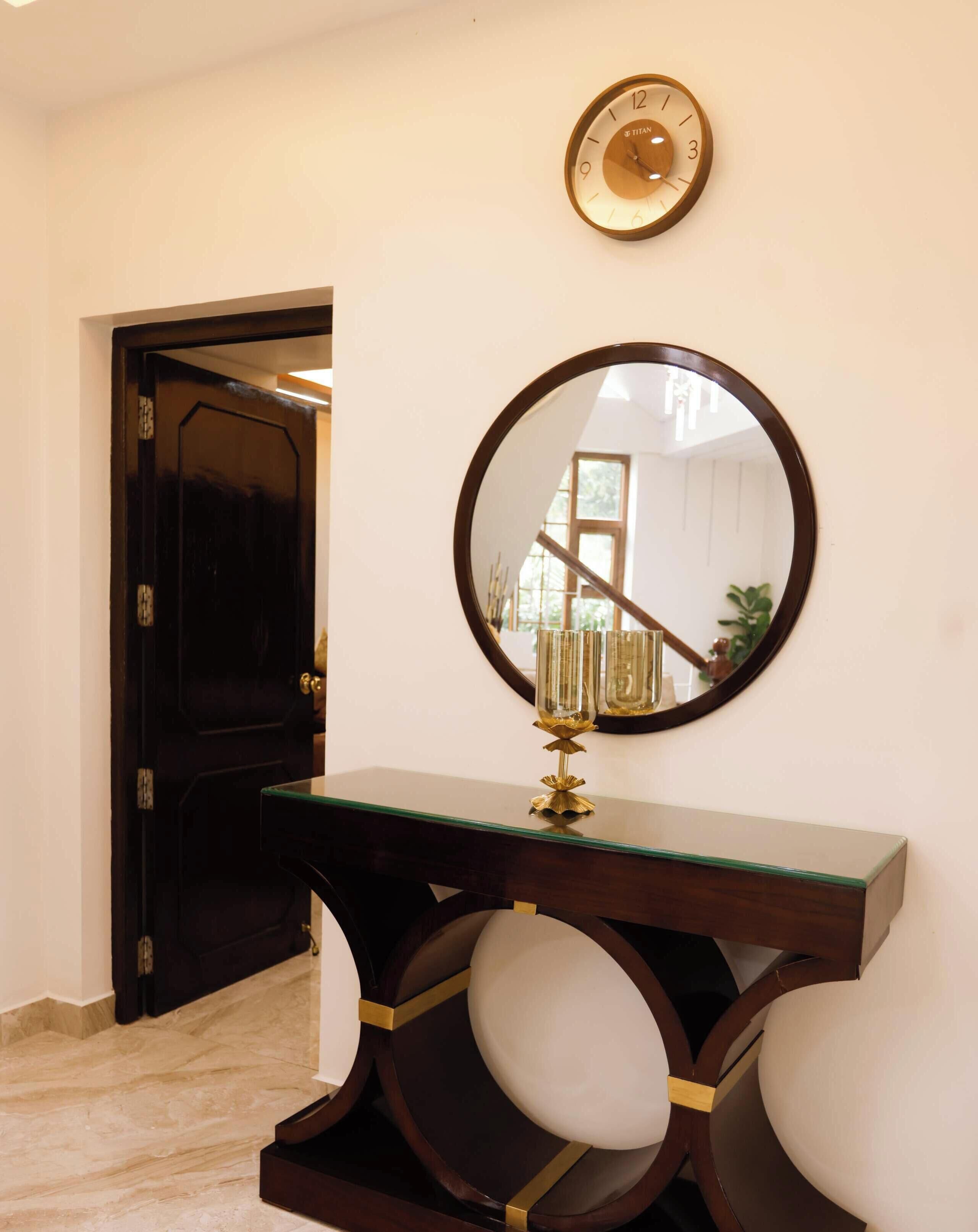 Un pasillo con una consola de madera oscura, un espejo redondo y un reloj de pared.