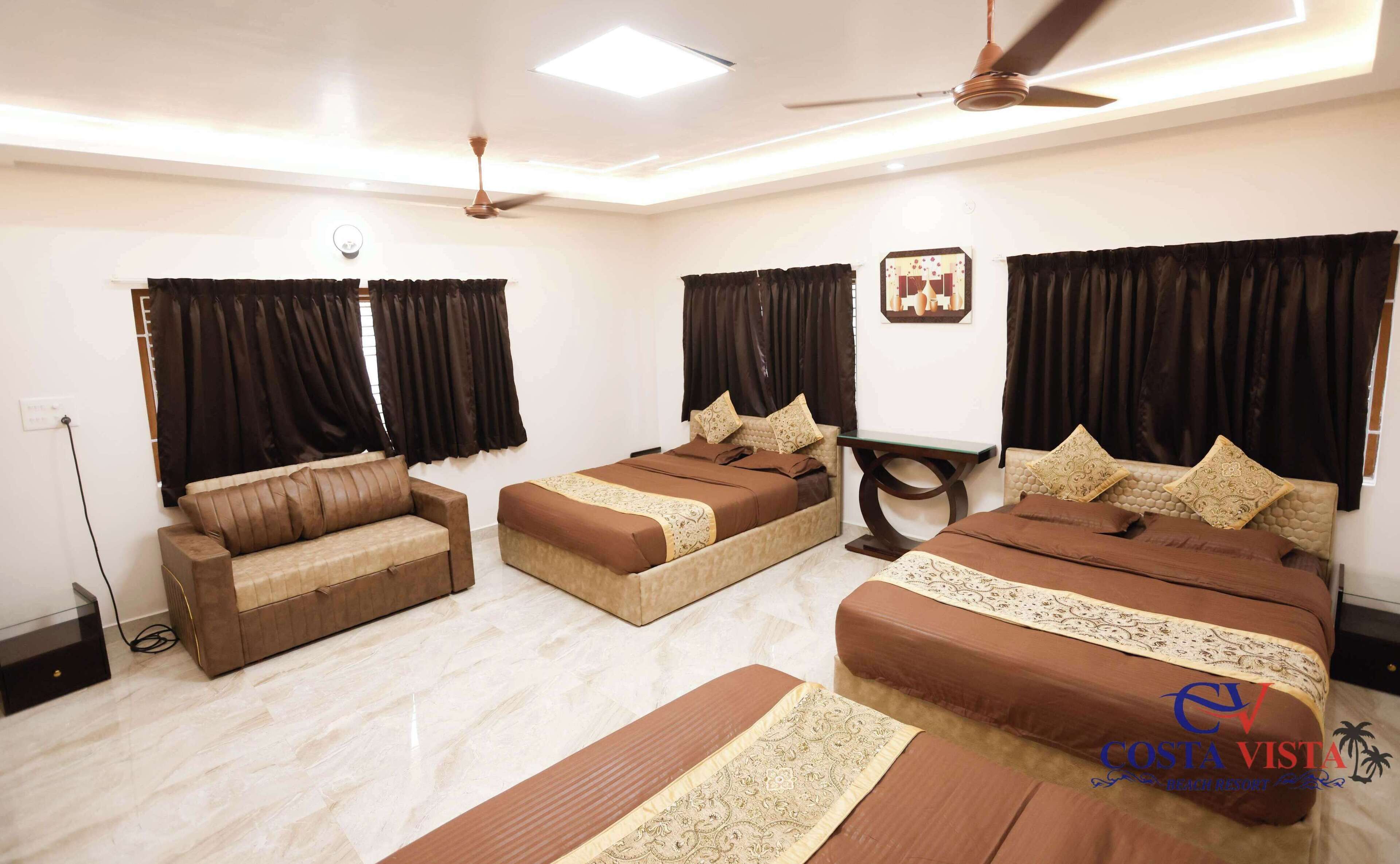 A hotel room with a sofa, two single beds, a ceiling fan, and a nightstand.