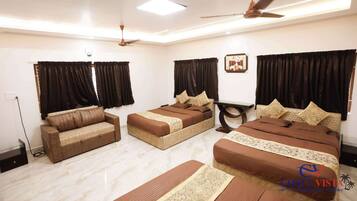 A hotel room with a sofa, two single beds, a ceiling fan, and a nightstand.