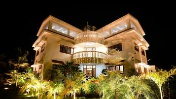 A multi-story building with a central circular balcony, surrounded by lush greenery and palm trees.