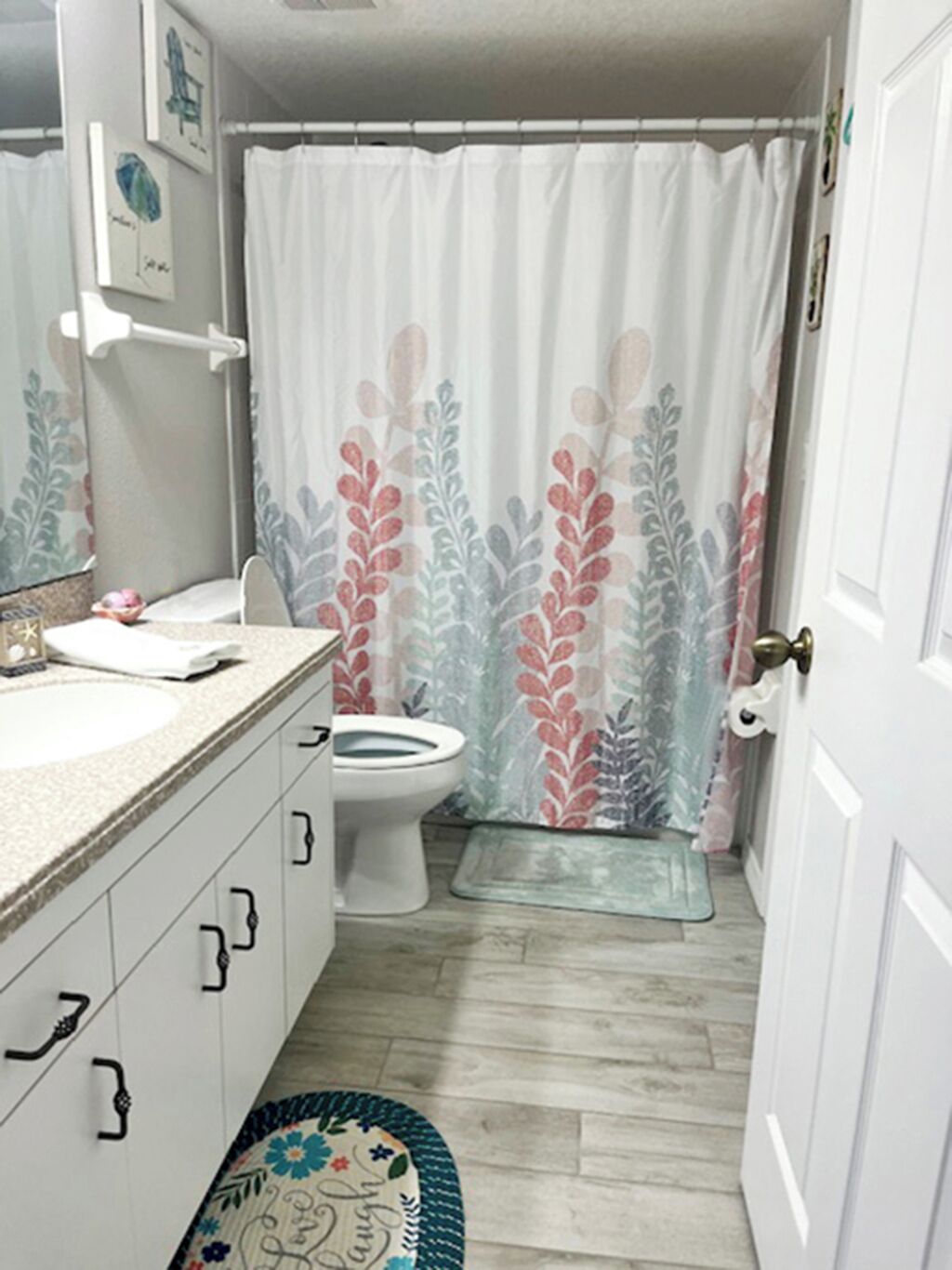 A bathroom with a toilet, a sink, a shower curtain with a floral pattern, and a decorative rug.