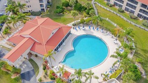 Luftaufnahme eines Hotels mit einem großen Schwimmbecken, umgeben von Liegestühlen und Palmen.