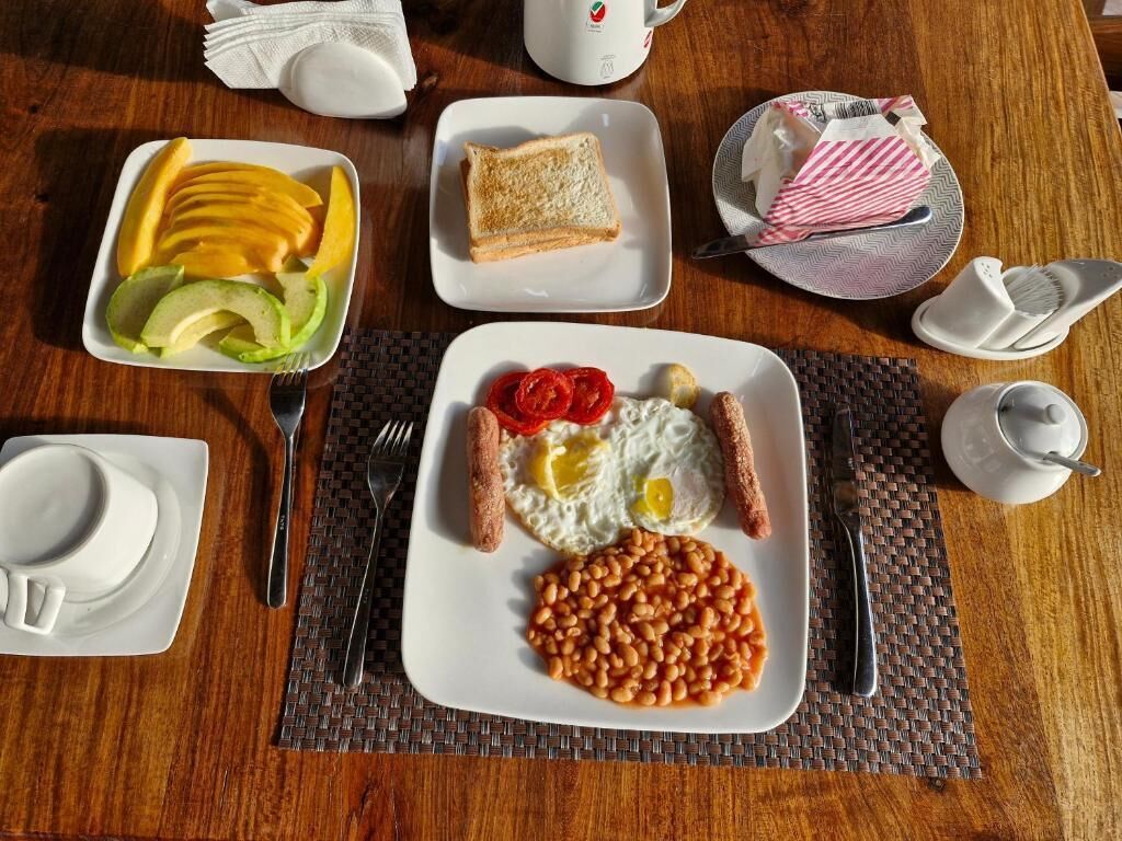 A breakfast setting with toast, eggs, sausages, beans, and fruit on a wooden table.