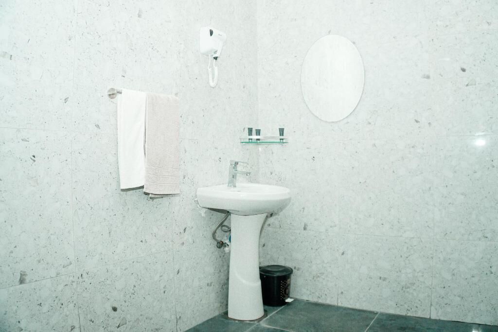Un baño con lavamanos blanco, una toalla colgada en la pared, un espejo y un cubo de basura.
