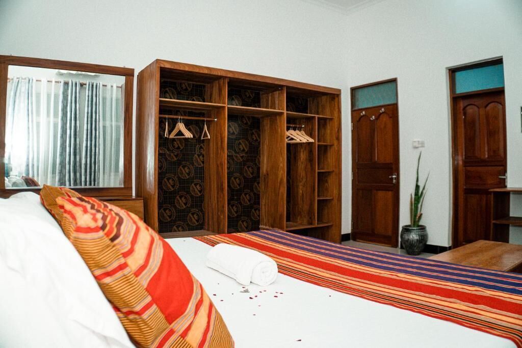 A hotel room with a bed, a large wooden wardrobe, and a potted plant.