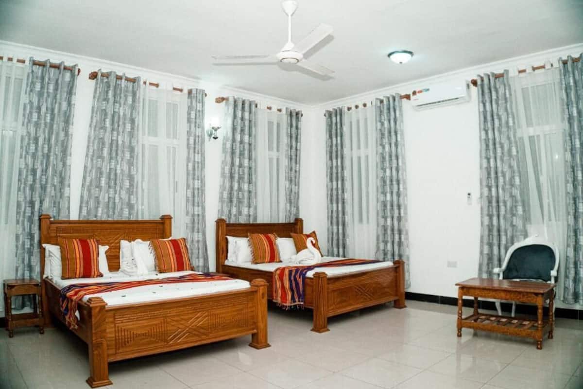 A room with two wooden beds, a ceiling fan, an air conditioning unit, and a small table.