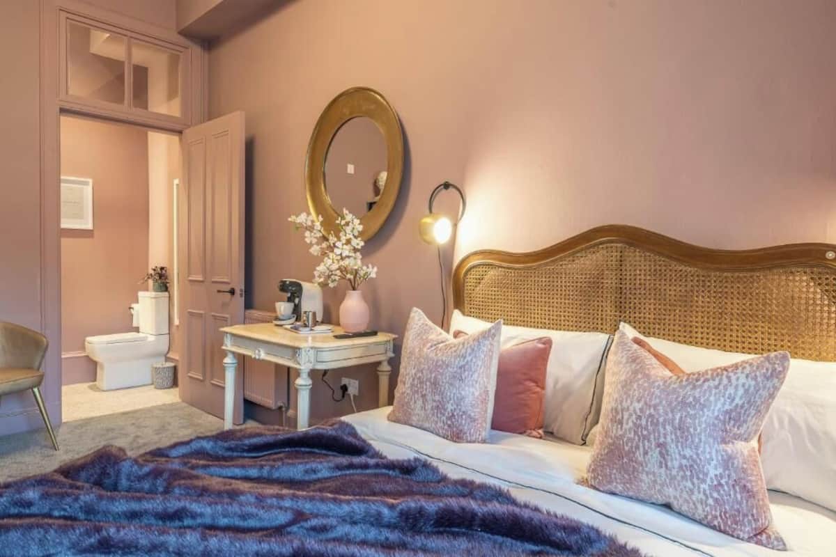 A bedroom with a bed, bedside table, lamp, and a mirror on the wall.