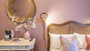 A hotel room with a bed, a bedside table with a coffee maker, a vase with flowers, and a round mirror on the wall. - Boutique Home Stay (Paisley)