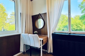 Une pièce comprenant une table à manger, des chaises, un miroir rond et une vue sur les arbres par une fenêtre.