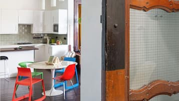 Una cocina moderna con armarios blancos, un comedor con sillas coloridas y una puerta de madera con mosquitera.