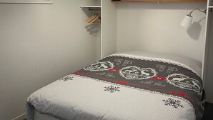 Un dormitorio pequeño y ordenado con una cama individual, un armario con espacio para colgar y un ventanal que proporciona luz natural.