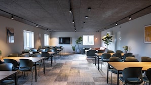 Une salle de conférence spacieuse, dotée de plusieurs tables et chaises, d’un téléviseur à écran plat et de plantes en pot.