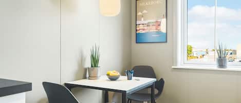 Een moderne eethoek met een tafel, stoelen, een hanglamp, een potplant en een lijst met een stadsbeeld.