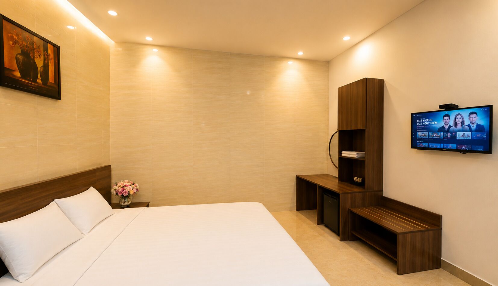 A hotel room with a large bed, a TV mounted on the wall, a wooden cabinet, and a small desk.
