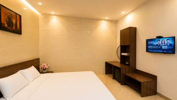 A hotel room with a large bed, a TV mounted on the wall, a wooden cabinet, and a small desk.